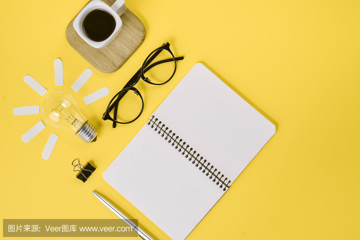 创意平铺概念顶视图的工作桌风格的设计办公用品与笔,记事本,眼镜,杯咖啡和灯泡在黄色的背景。概念的头脑风暴